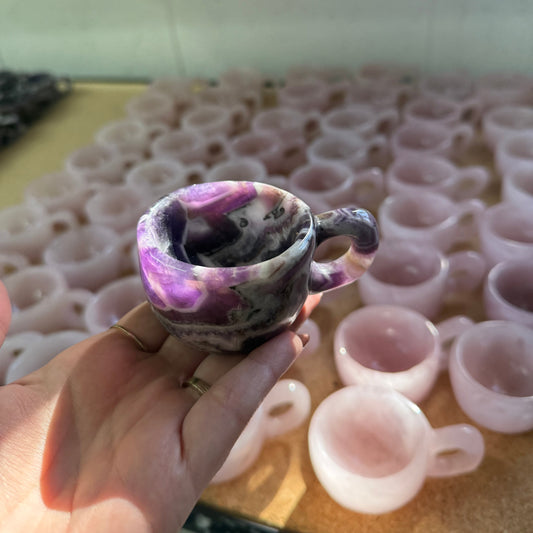 Hand holding a purple and white ceramic cup with a textured surface, against a background of similar cups.