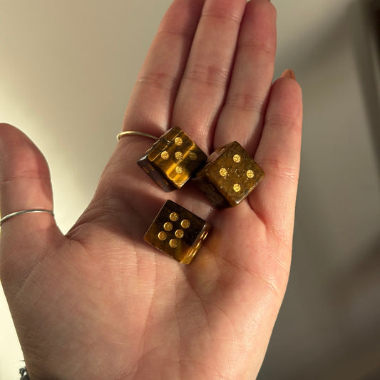 Three tiger's eye crystal dice with gold pips rest in an open palm.