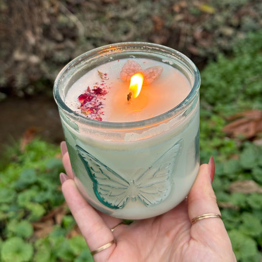 Hand holding a lit candle in a decorative glass container against a natural background