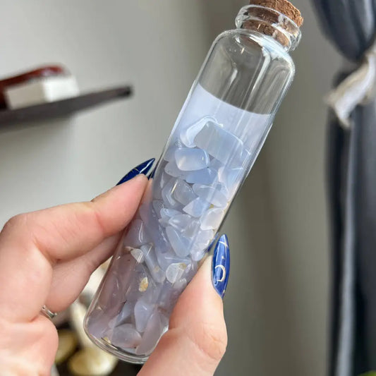 Hand holding clear glass bottle with cork, ice water, blue nail polish