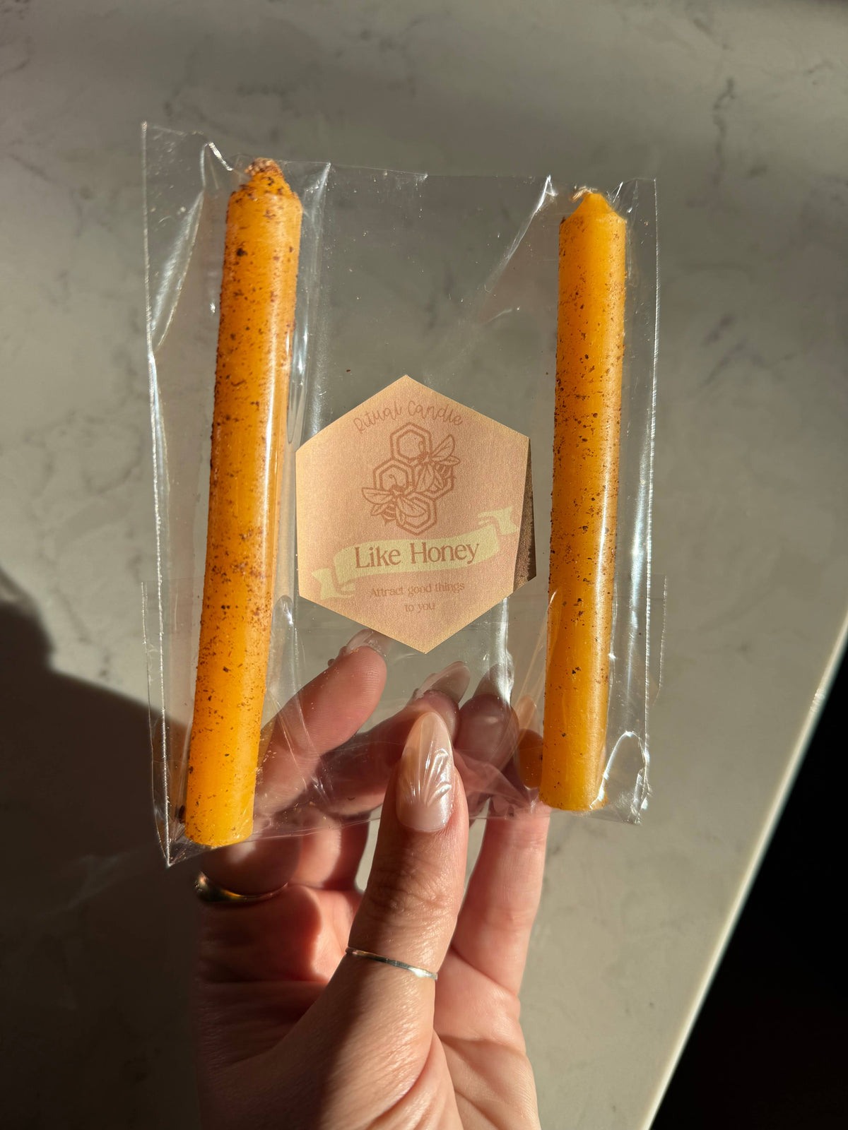 Two honey orange taper candles in a clear sleeve with a Like Honey Ritual Candle label