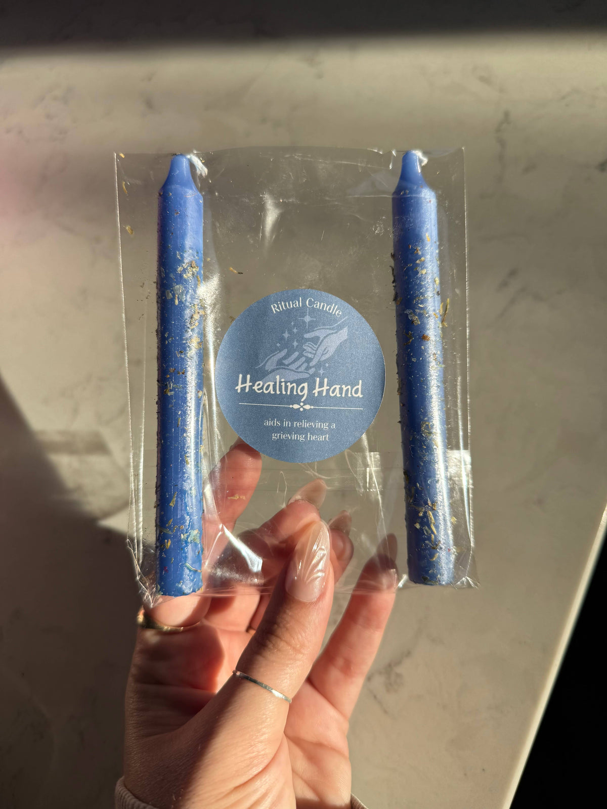 Two blue taper candles in a clear sleeve with a Healing Hand Ritual Candle label
