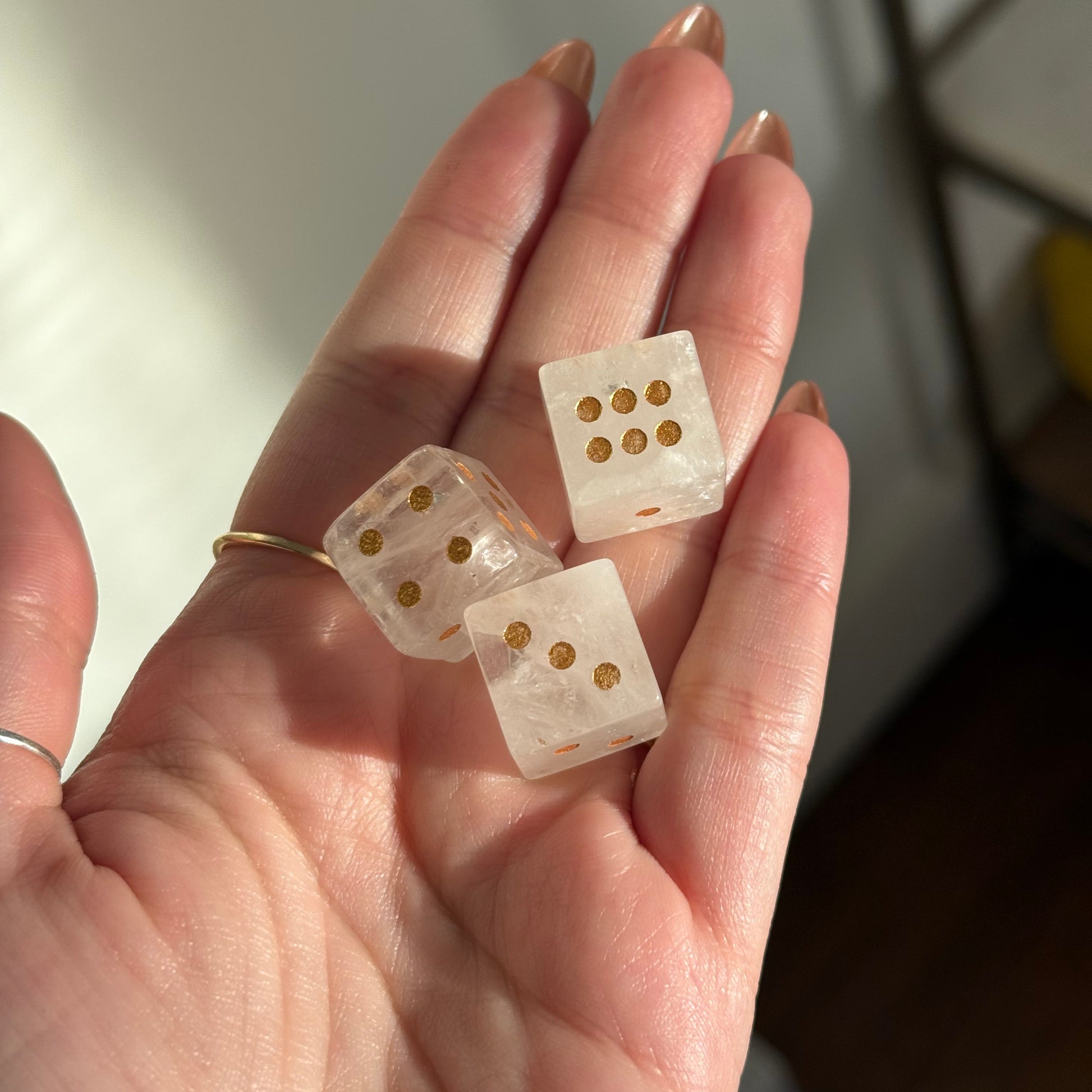 Three clear crystal dice with gold dots are held in a hand.