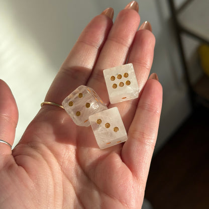 Three clear crystal dice with gold dots are held in a hand.