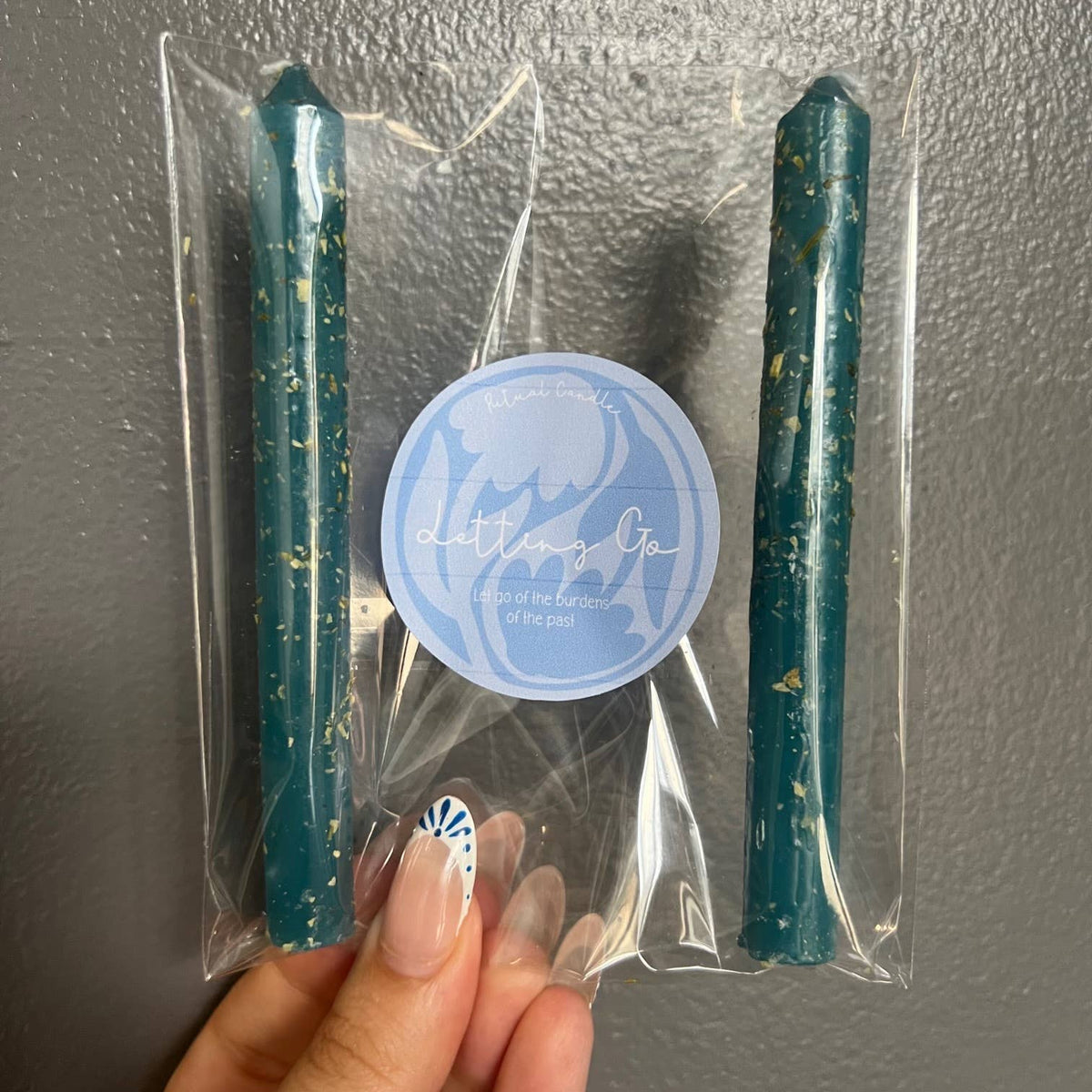 Two teal taper candles in a clear sleeve with a Letting Go Ritual Candle label