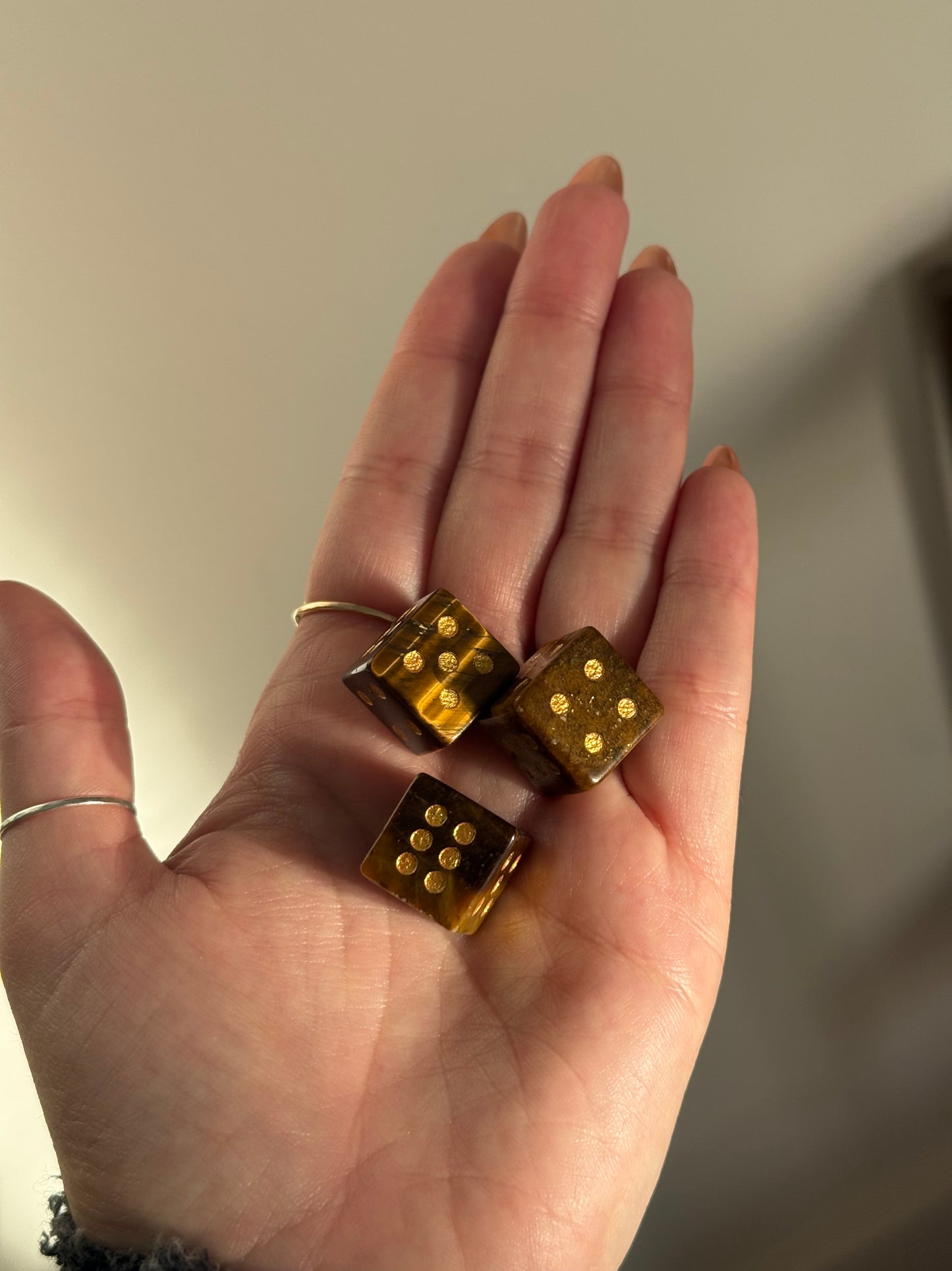 Three tiger's eye crystal dice with gold pips rest in an open palm.