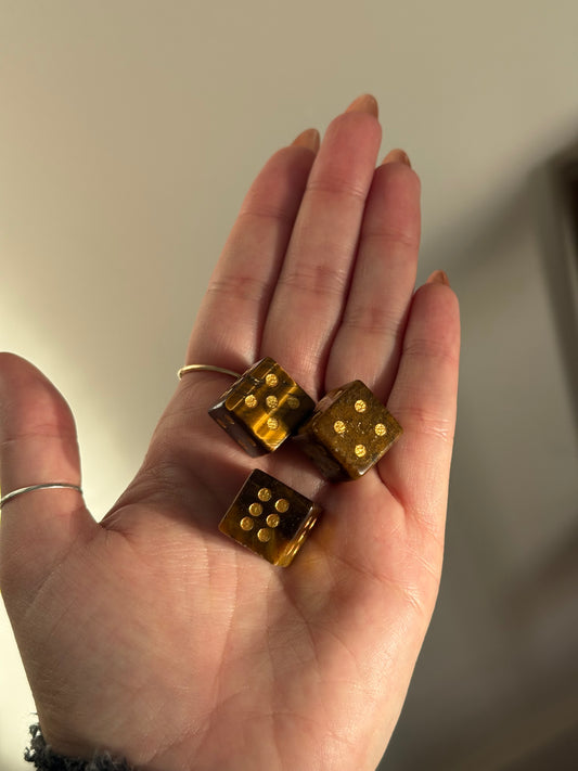 Three tiger's eye crystal dice with gold pips rest in an open palm.