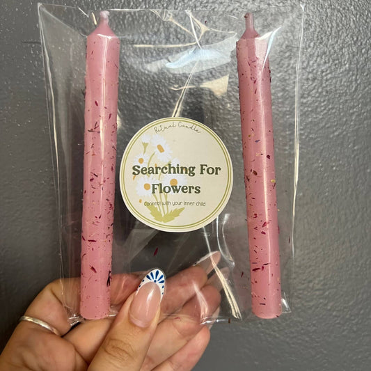 Two pink taper candles in a clear sleeve with a Searching for Flowers Ritual Candle label