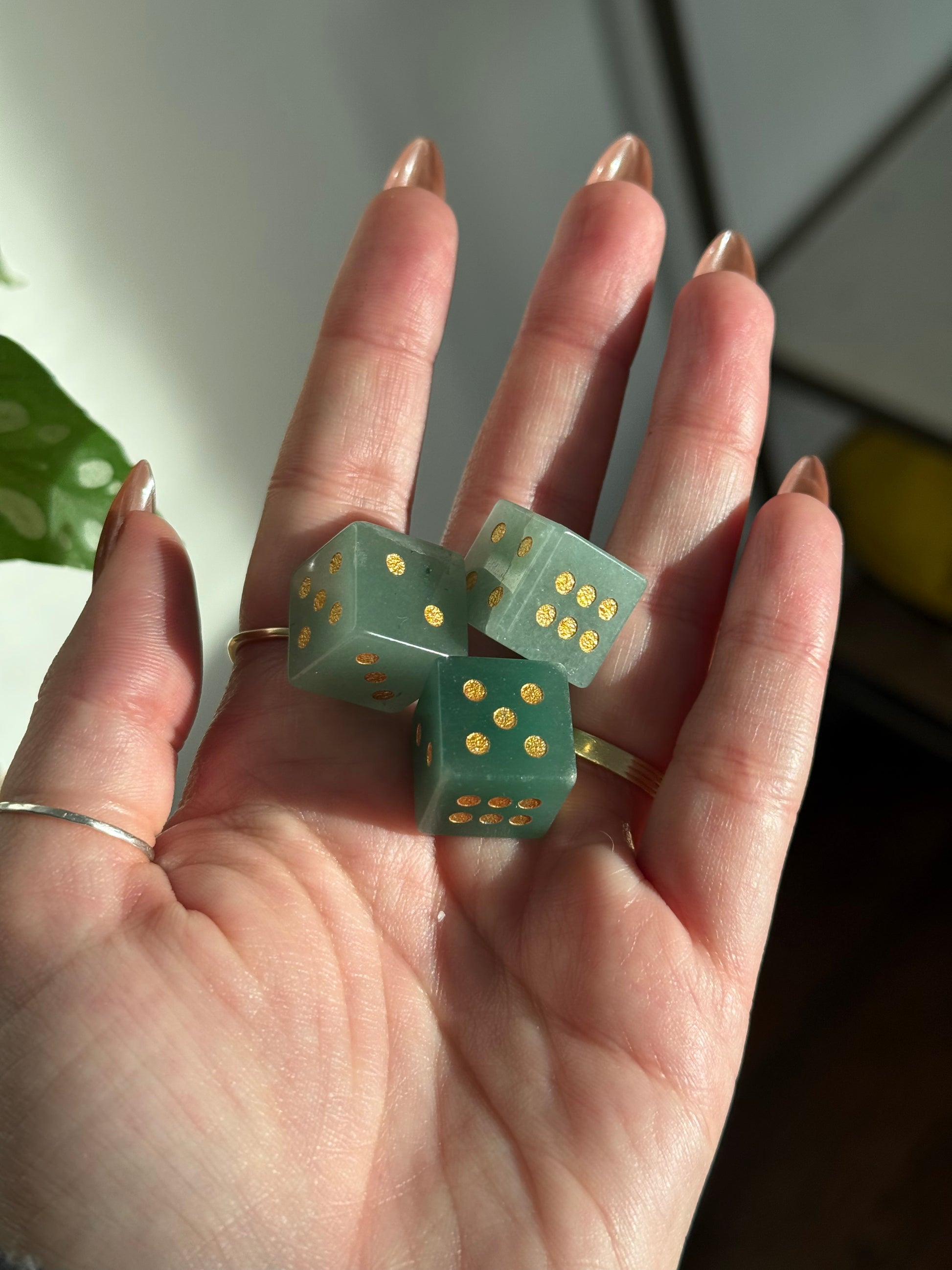 Three green crystal dice with gold dots rest in an open palm.