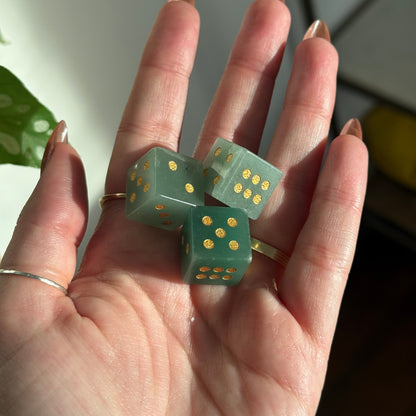 Three green crystal dice with gold dots rest in an open palm.