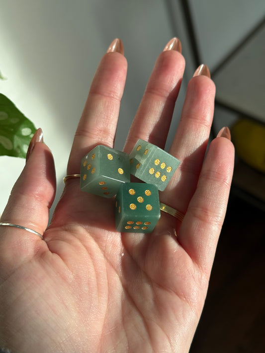 Three green crystal dice with gold dots rest in an open palm.