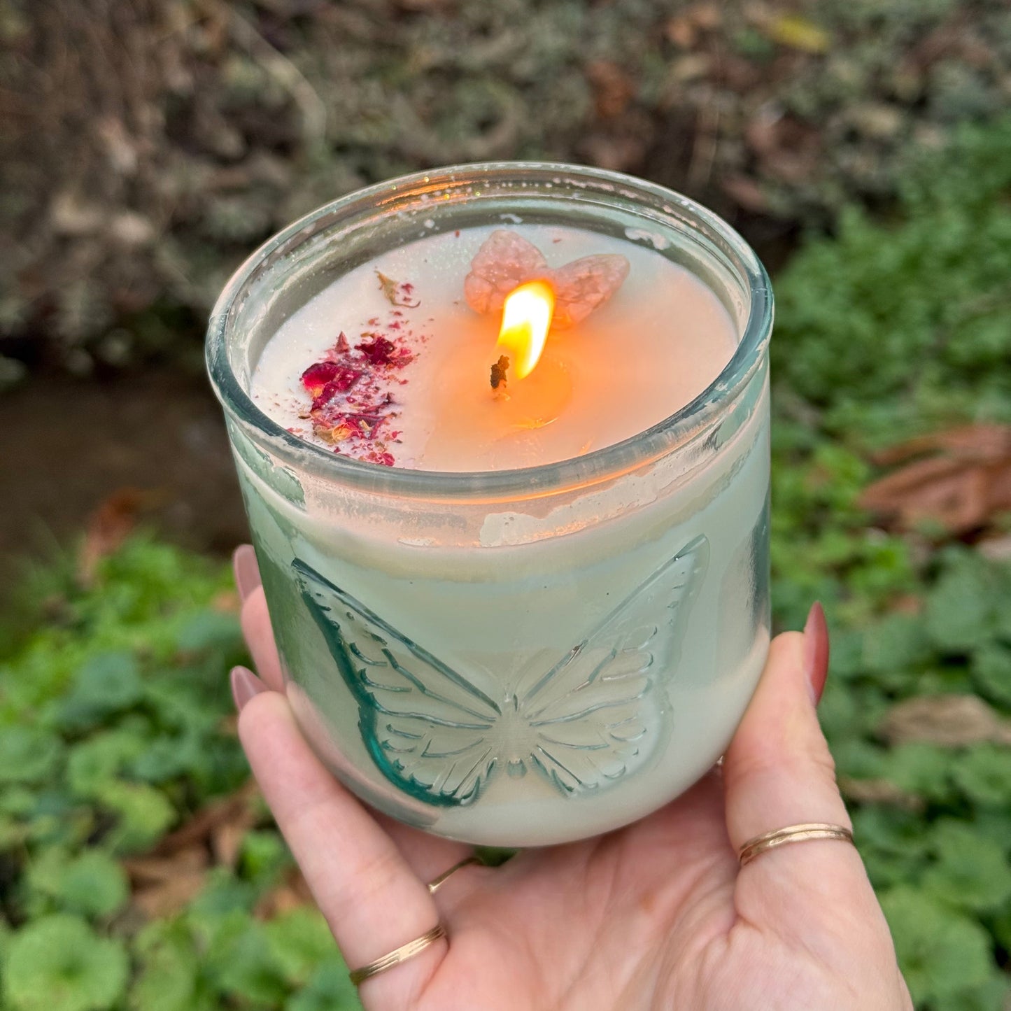 Hand holding a lit candle in a decorative glass container against a natural background