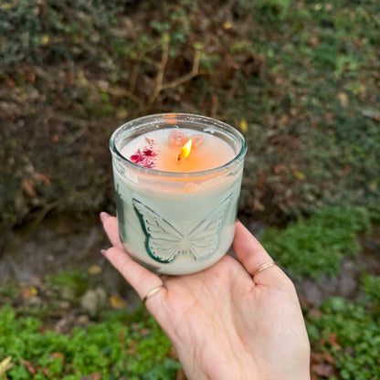 Hand holding a lit candle with a leaf design against a natural background