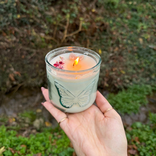 Hand holding a lit candle with a leaf design against a natural background