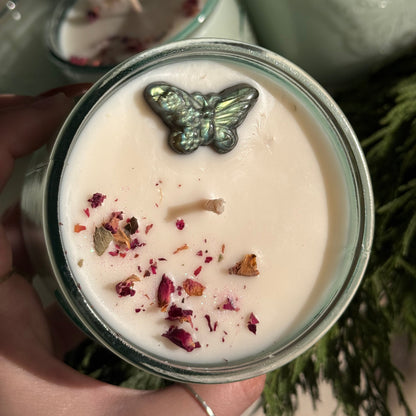 Candle with decorative elements held by a hand, with more candles in the background.