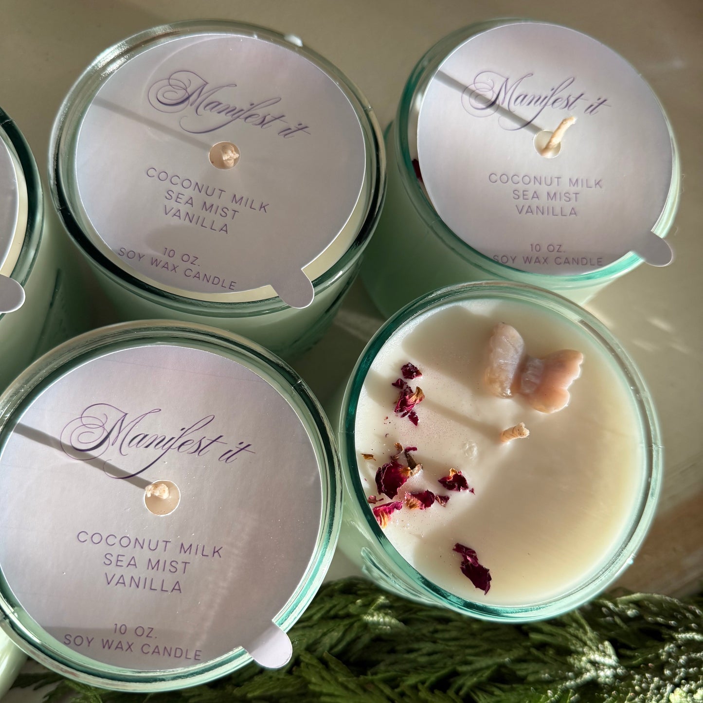 Four candles in green tins with visible labels on a surface with greenery.