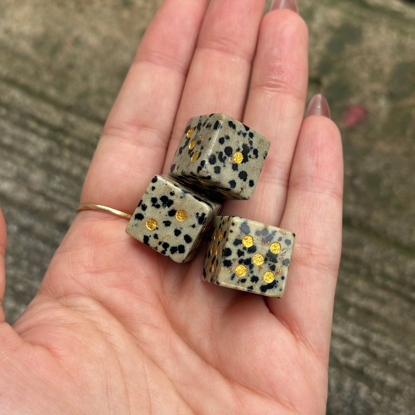 Hand holding three dice with spotted pattern and gold dots against a blurred natural background