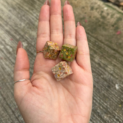 Hand holding three small, rough-textured stones on a concrete surface