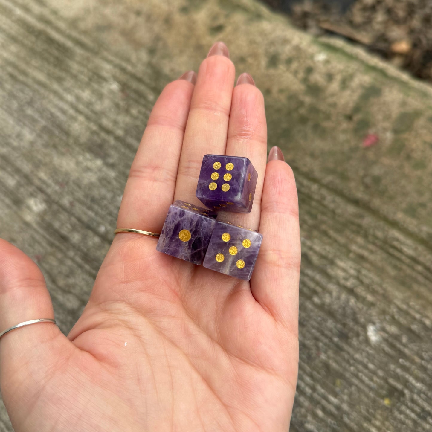 Hand holding two purple dice with gold pips on a concrete surface