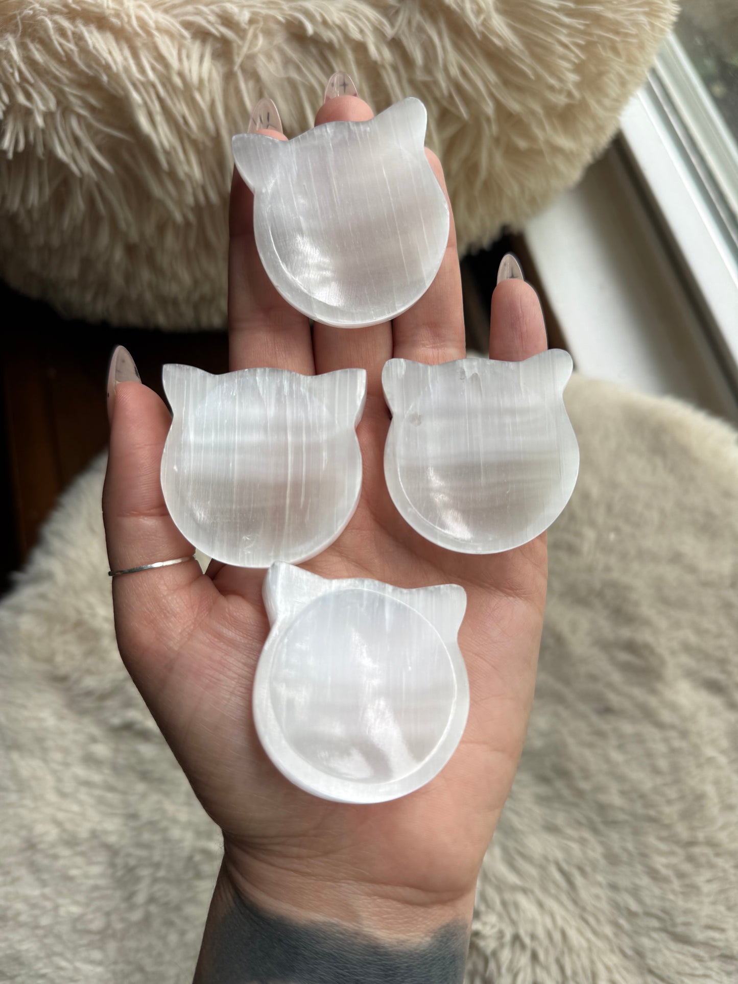 Four selenite cat bowls held in a hand showing natural variation