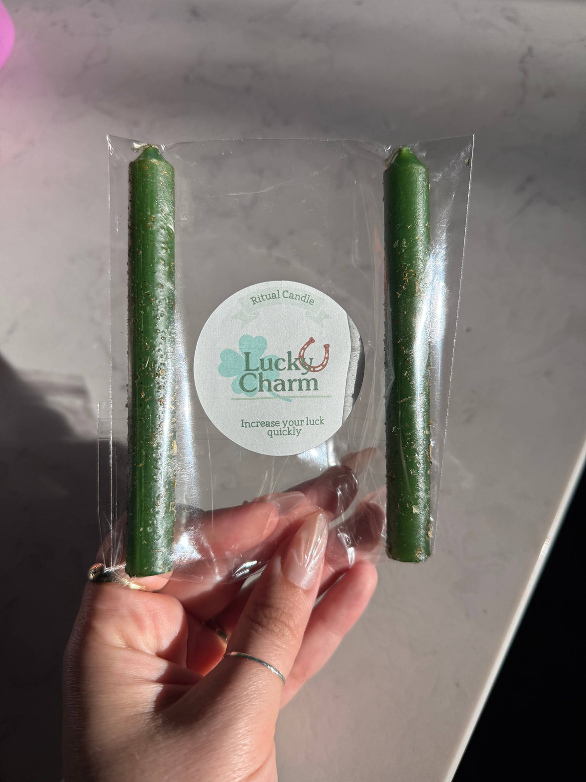 Two green taper candles in a clear sleeve with a Lucky Charm Ritual Candle label