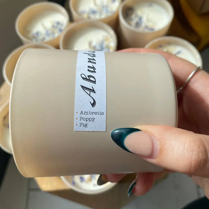 Beige frosted glass 10 oz soy candle with Abund label, ambrette poppy fig scents