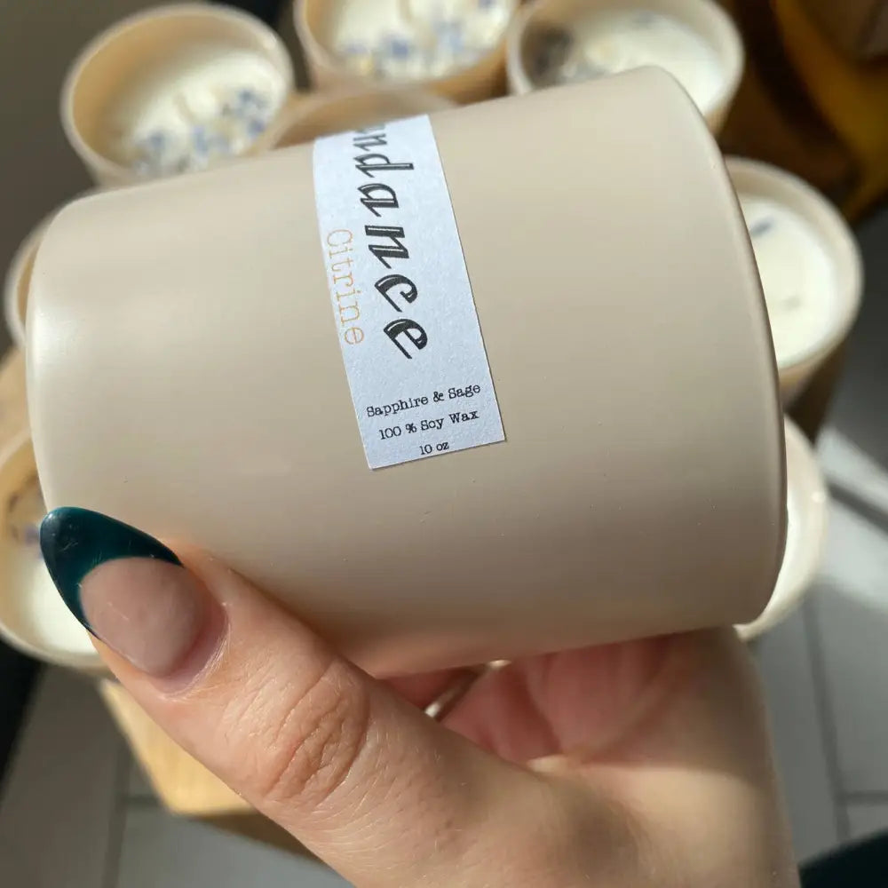 Beige matte Abundance candle with blue nail polish in 10 oz soy wax jar