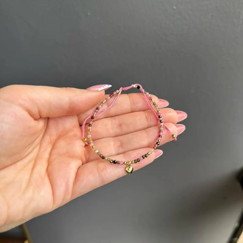 Pink adjustable crystal gemstone bracelet with heart charm, gold accents, and bells