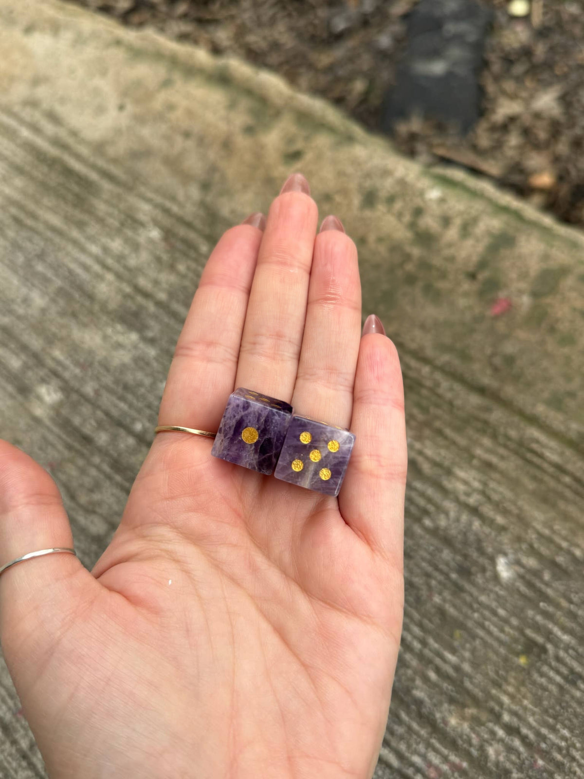 Two amethyst crystal dice with gold pips in an open palm