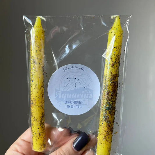 Yellow speckled Aquarius zodiac taper candle in clear pack with herbs and oils