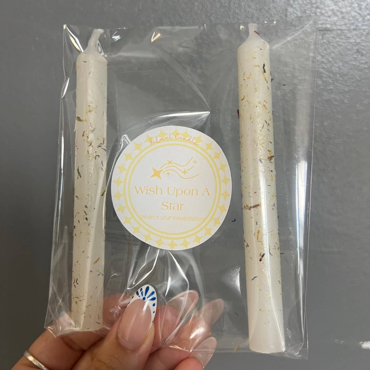 Two white herb-dressed taper candles in a clear sleeve with a Wish Upon a Star Ritual Candle label