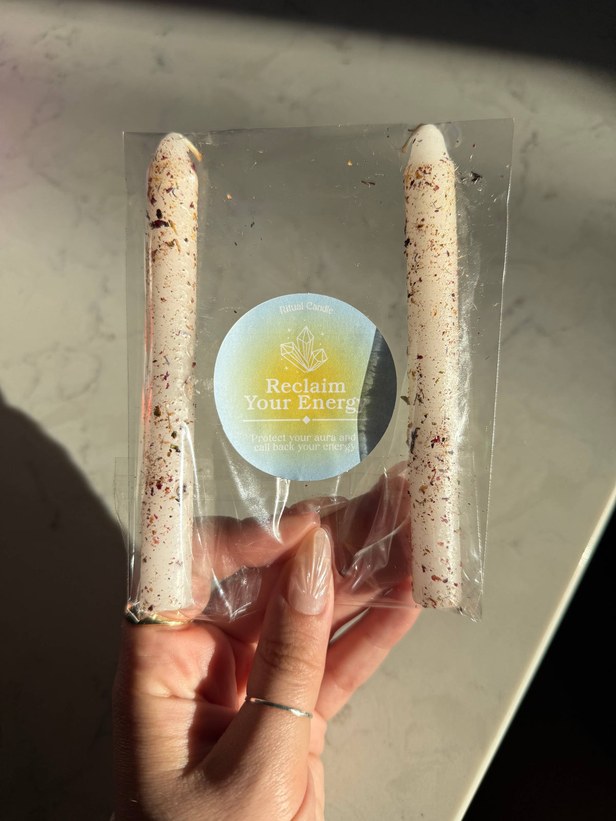 Two cream herb-dressed taper candles in a clear sleeve with a Reclaim Your Energy Ritual Candle label