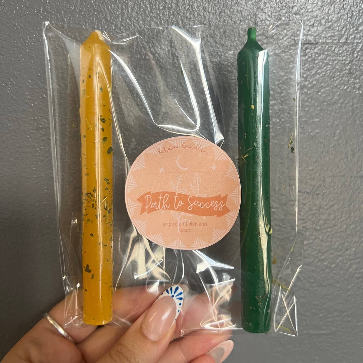 One yellow and one green taper candle in a clear sleeve with a Path to Success Ritual Candle label