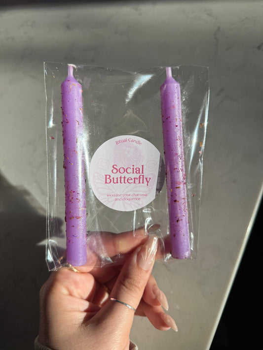 Two lavender taper candles in a clear sleeve with a Social Butterfly Ritual Candle label