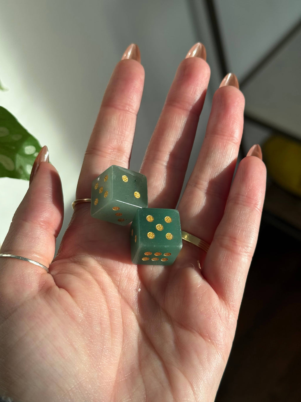 Two green aventurine crystal dice with gold pips in an open palm