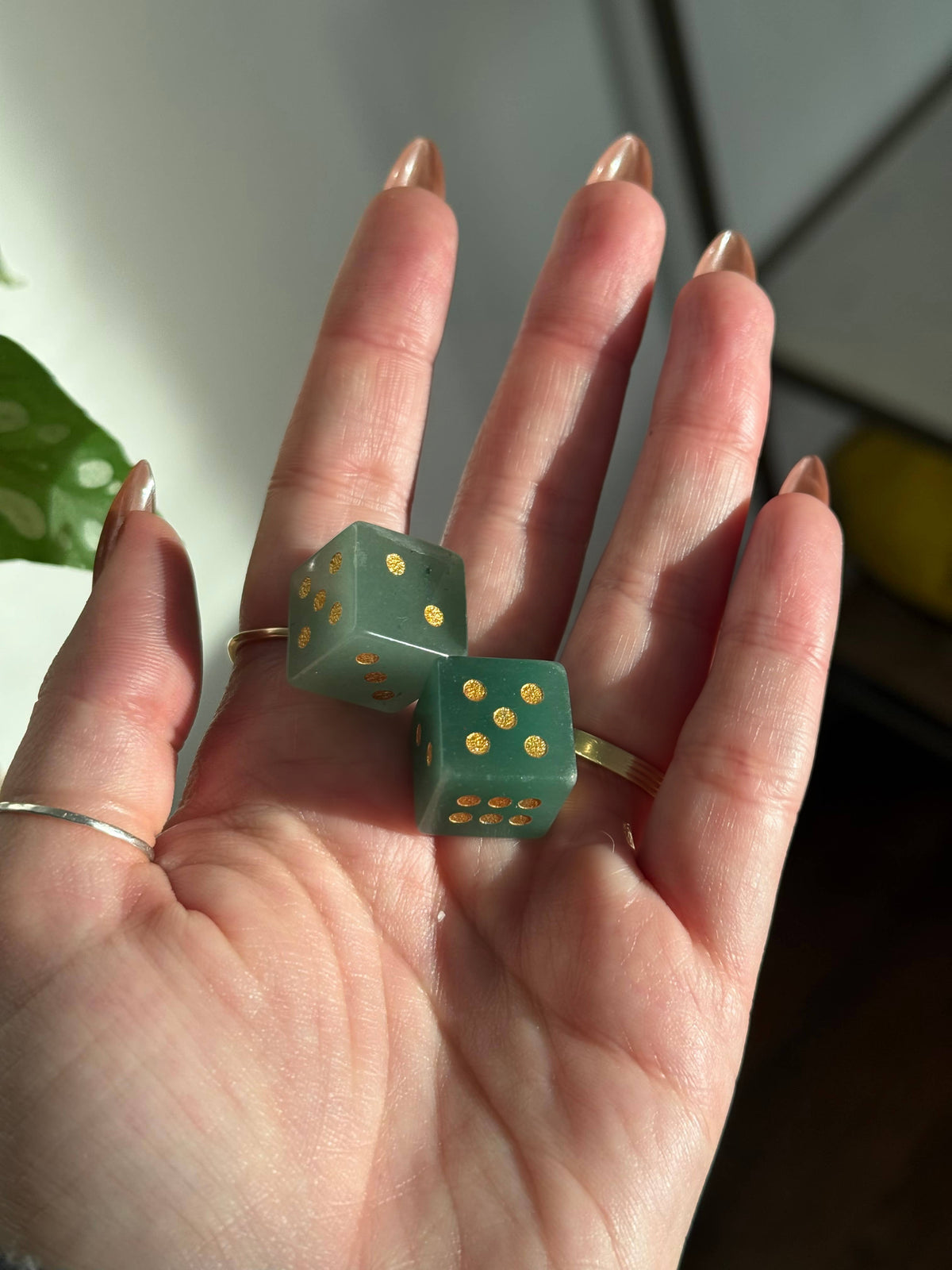 Two green aventurine crystal dice with gold pips in an open palm