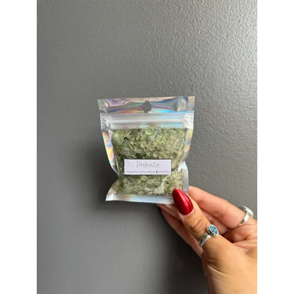 Hand holding clear bag of premium crystal chip stones in dried green herbs