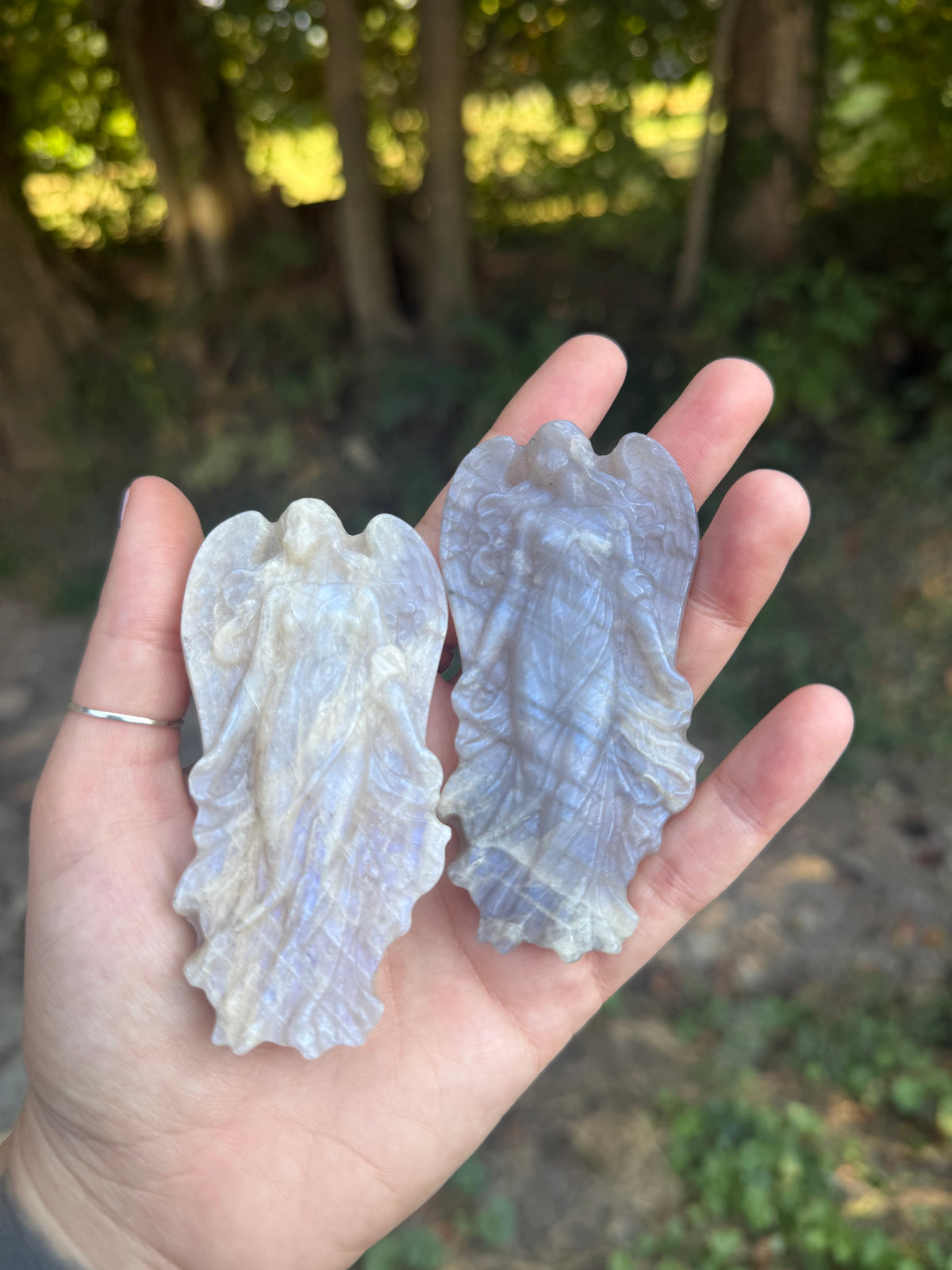 Two moonstone angel carvings, one whiter and one greyer, held outdoors
