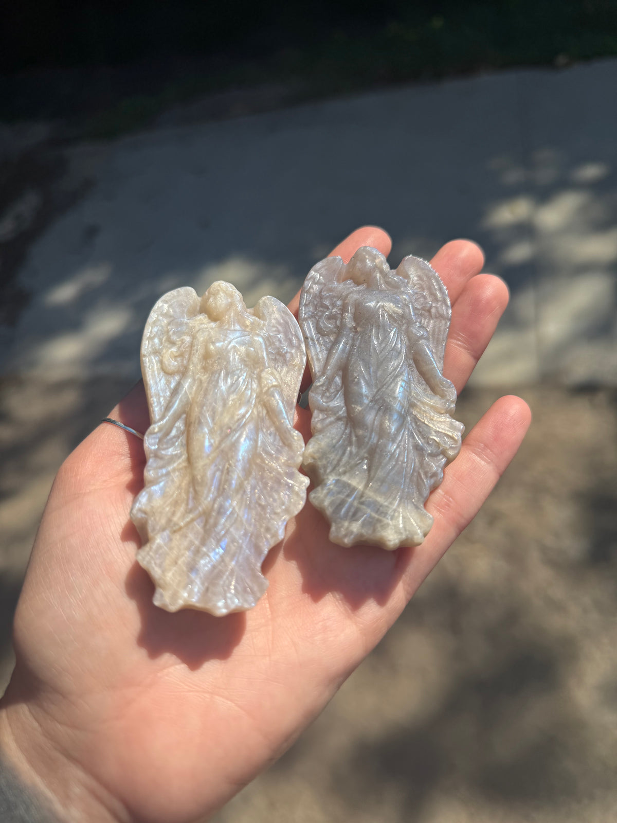Two moonstone angel carvings in sunlight showing natural color variation