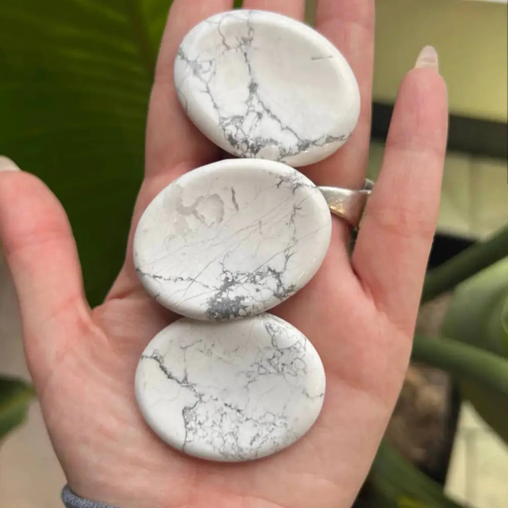 Hand holding white marble-like worry stone pendant with gray veining, 2 inches