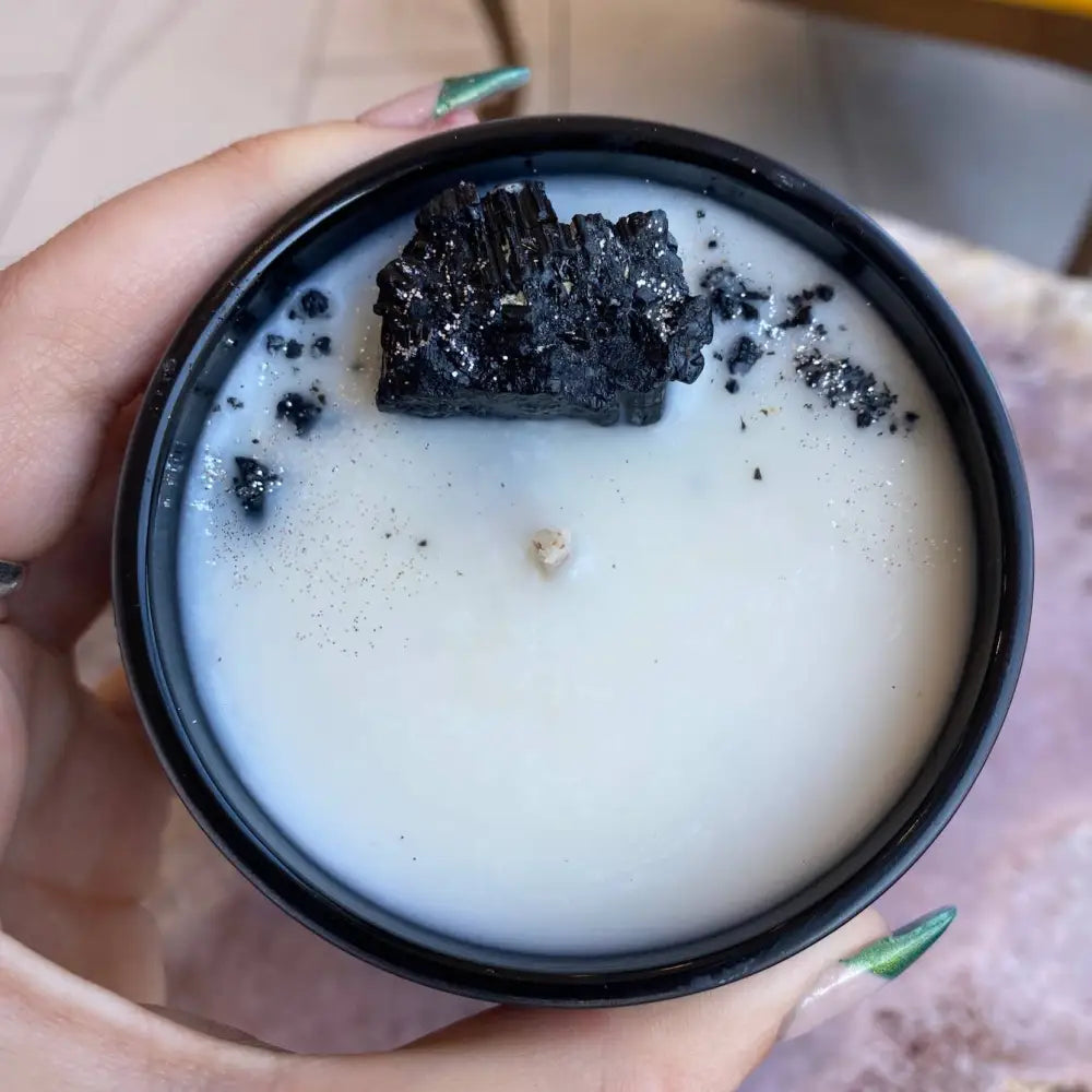 Hand holding white soy wax candle with black rock decor and green nails, 10oz black jar
