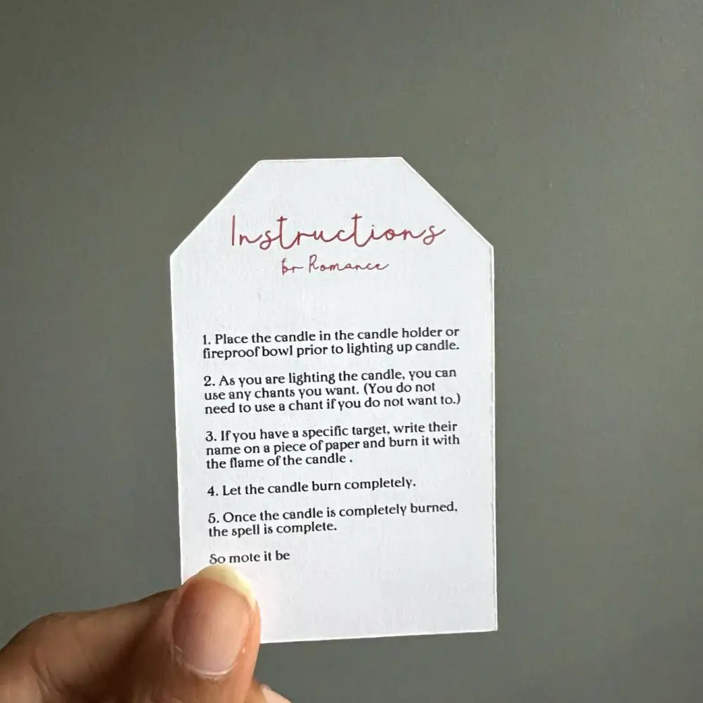 White paper tag with pink cursive romantic spell text and black instructions for Romance Ritual Candle Set