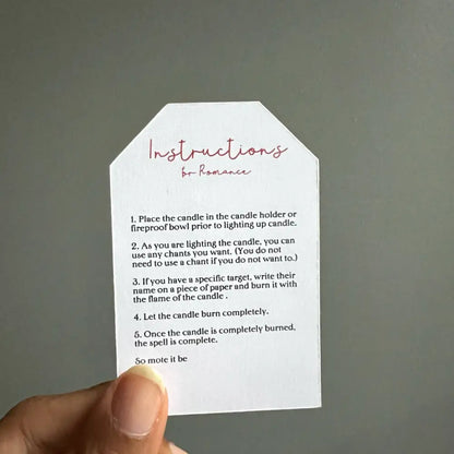 White paper tag with pink cursive romantic spell text and black instructions for Romance Ritual Candle Set