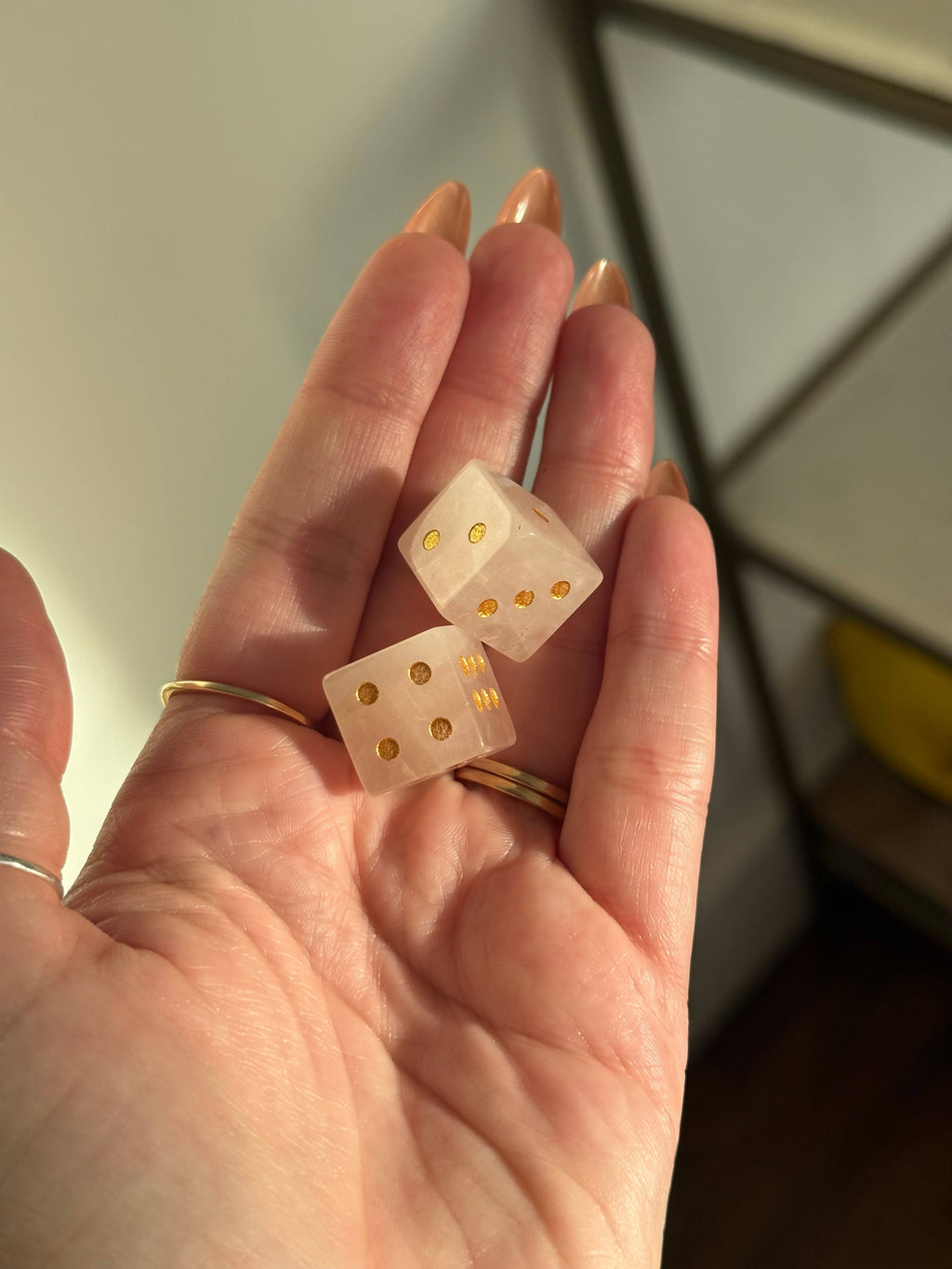 Two rose quartz crystal dice with gold pips in an open palm