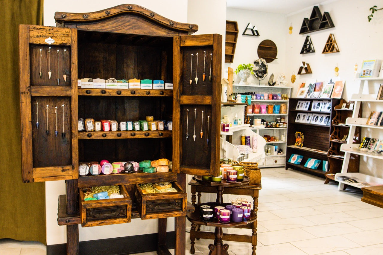 Inside the Sapphire and Sage Nashville store, a carved wooden cabinet of candles and crystals with pendulums in its open doors